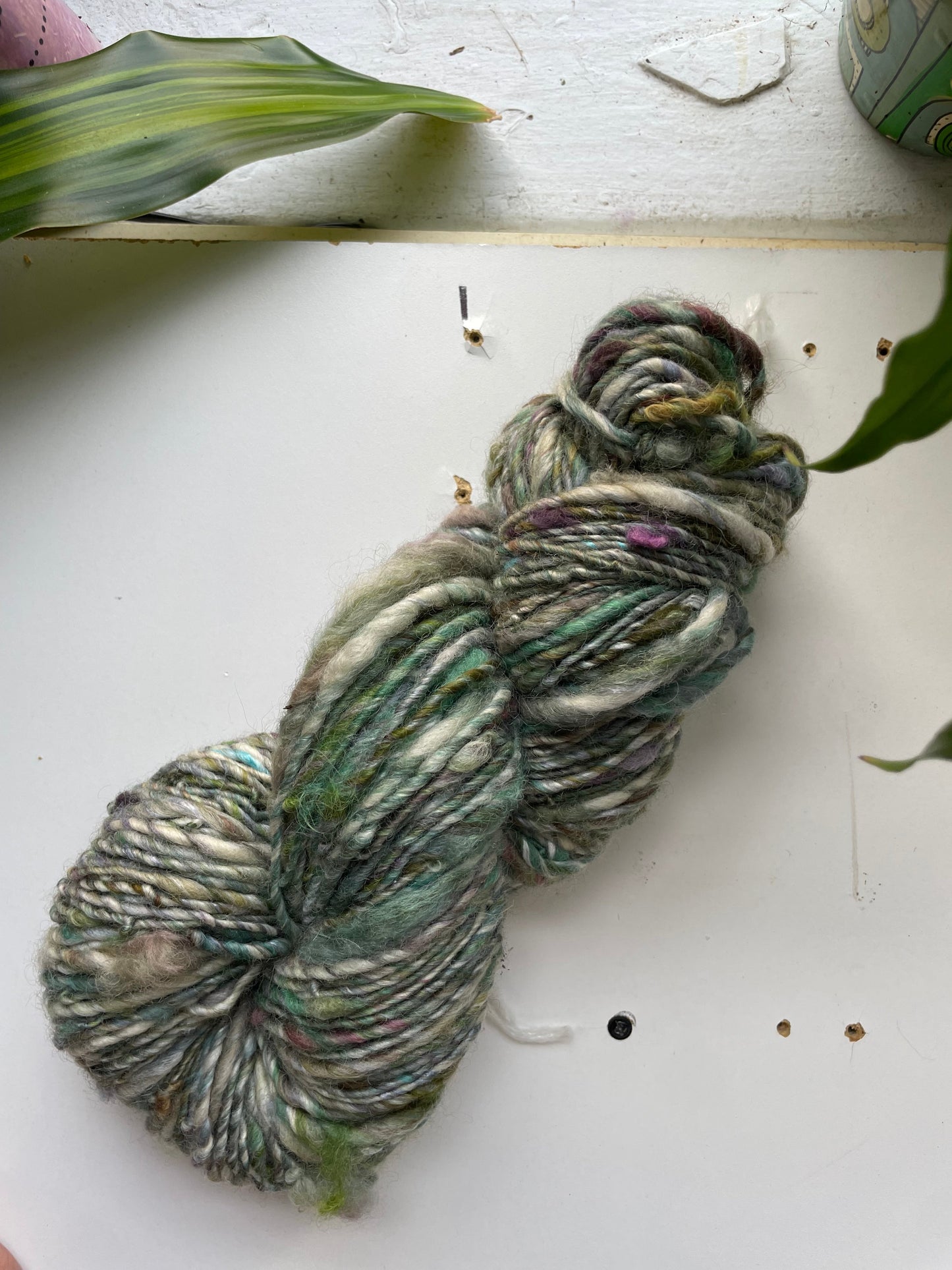 Green and gray skein of yarn on a white surface with leaves.