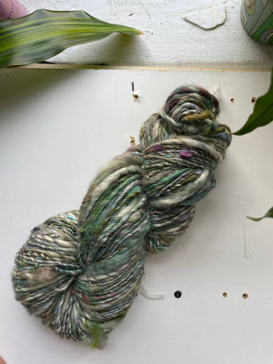 Green and gray skein of yarn on a white surface with leaves.